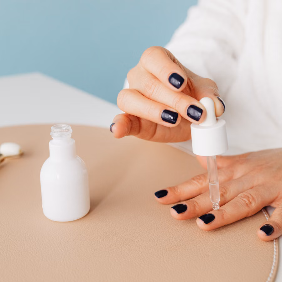 Close-up of a woman applying nail oil with a dropper for manicure care on blue background.