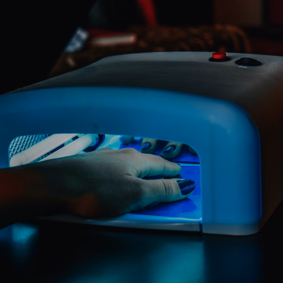 A hand with manicured nails being cured under a blue LED lamp for gel polish.